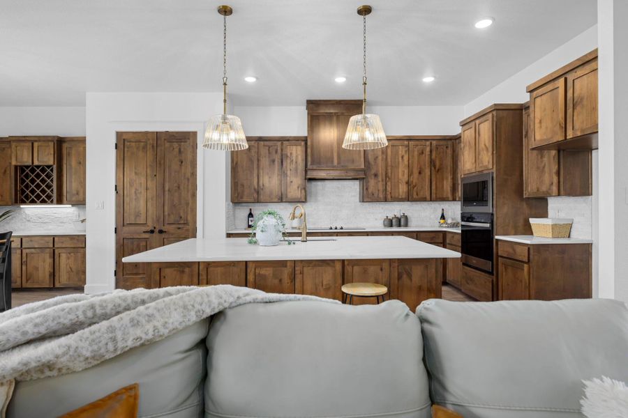 Kitchen featuring an island with sink, stainless steel appliances, open floor plan, backsplash, and decorative light fixtures
