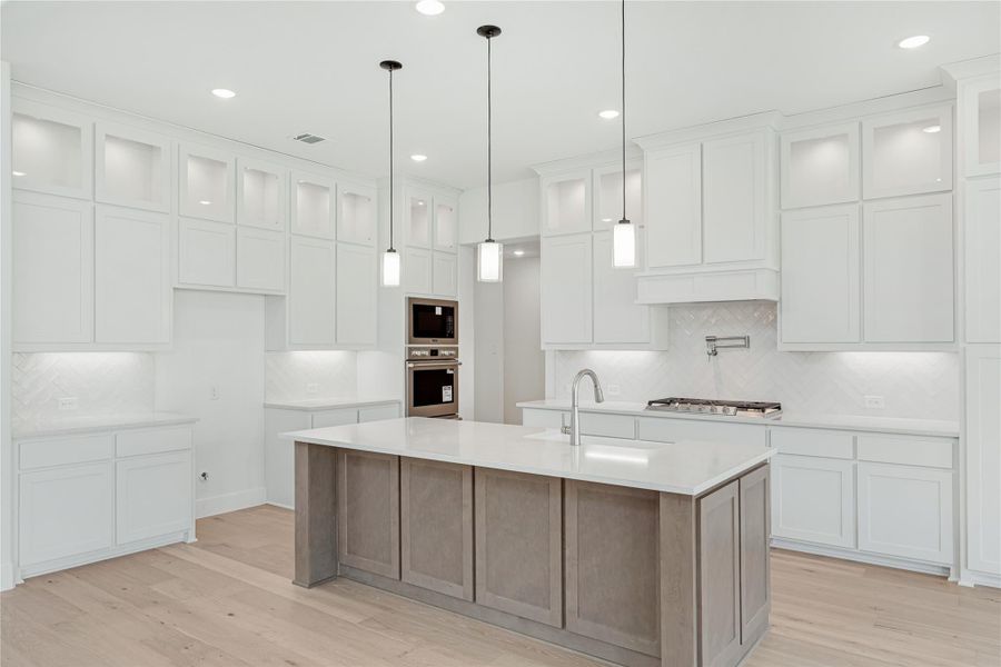 White kitchen with large center island, pendant lights, double ovens, and light hardwood floors