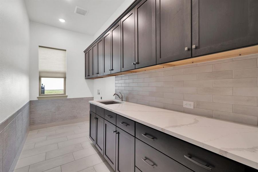 Washroom with a wainscoted wall, light tile patterned floors, tile walls, hookup for a washing machine, and cabinet space