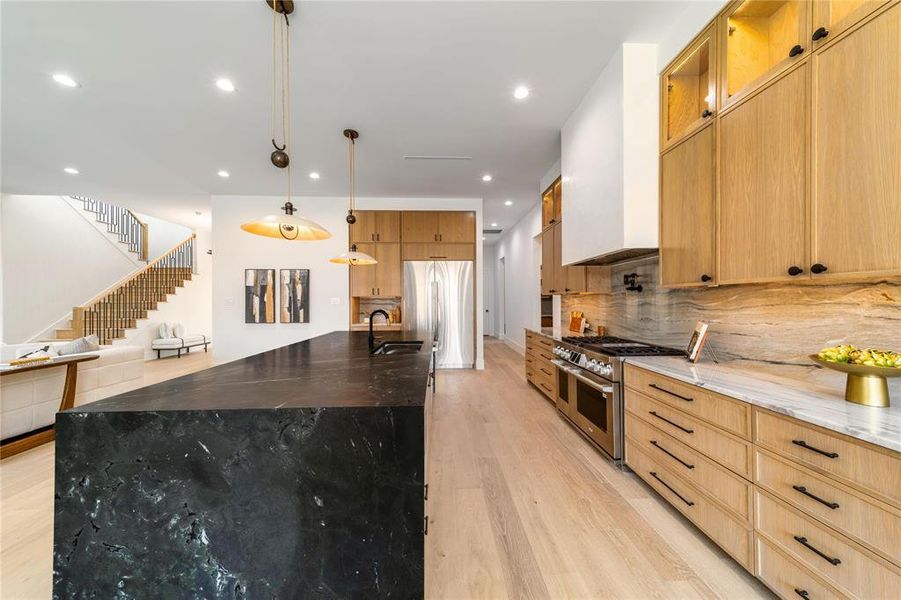 Kitchen with dark stone counters, stainless steel appliances, hanging light fixtures, light wood-style floors, and a spacious island
