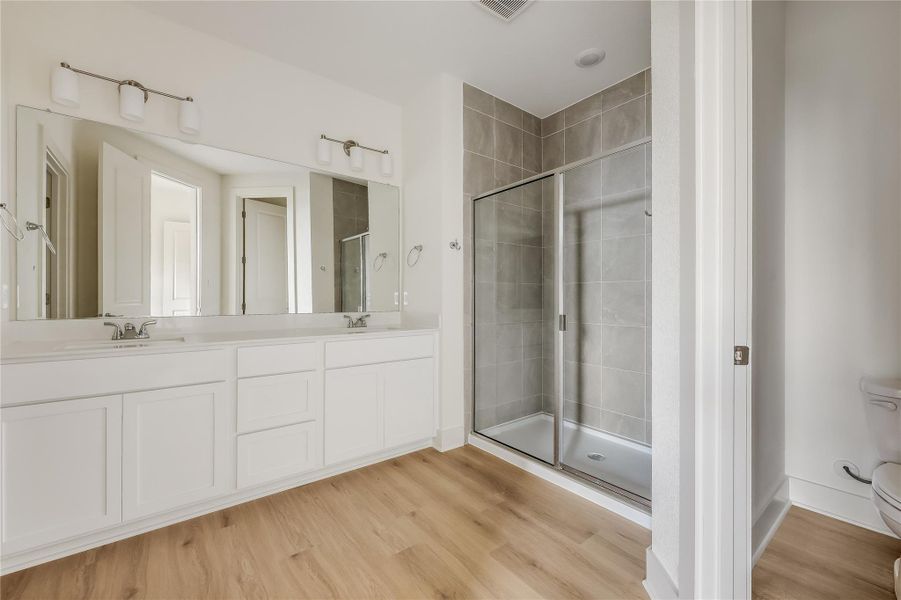 Full bathroom featuring a shower stall, double vanity, and light wood-style floors