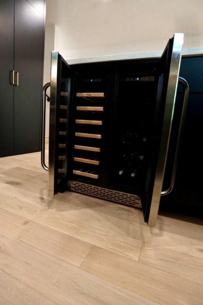 Kitchen view of wine cooler, dark cabinets, and light wood-type flooring