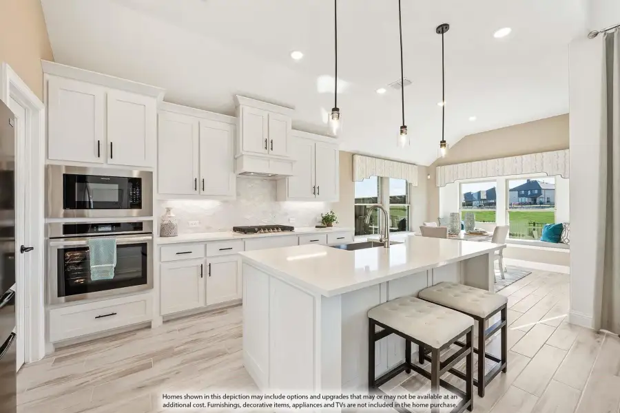 Kitchen with white cabinets, large island with seating, stainless steel appliances, and pendant lights over light wood floors