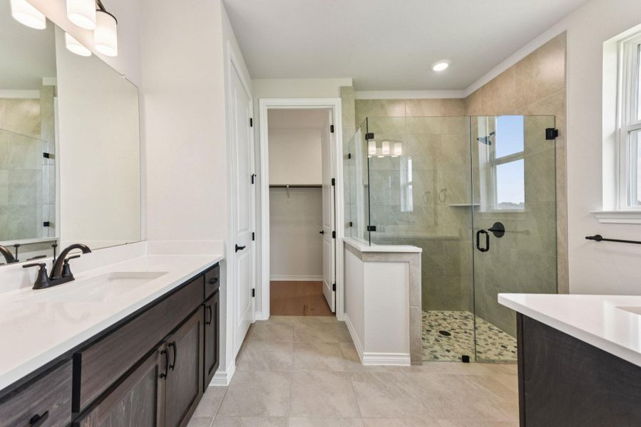 Full bath featuring two vanities, a shower stall, light tile patterned floors, and a walk in closet