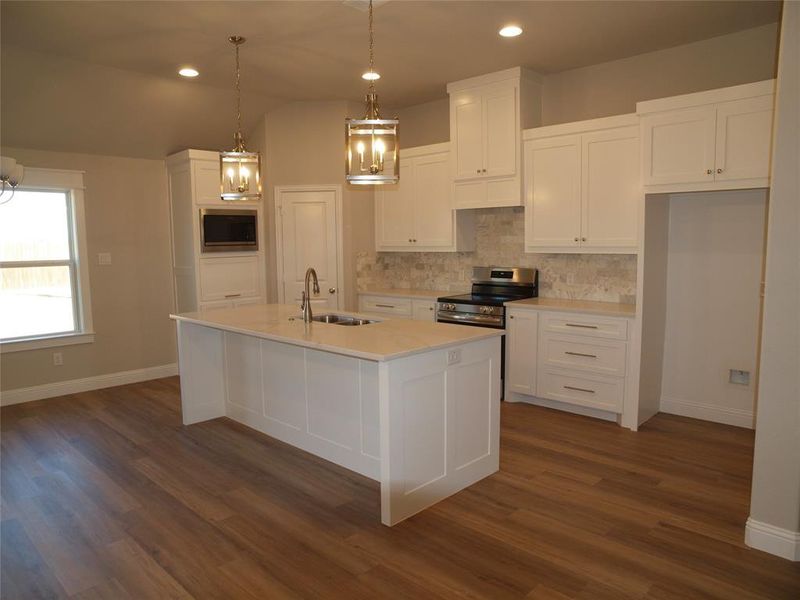 Kitchen with sink, appliances with stainless steel finishes, a kitchen island with sink, white cabinetry, and decorative light fixtures