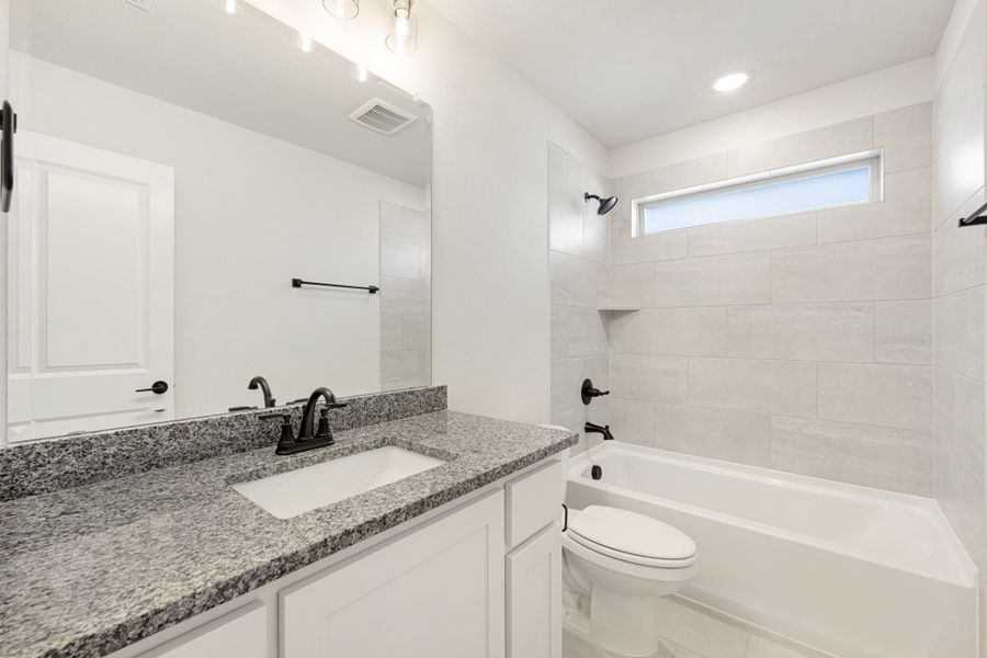 Bathroom with granite countertop, white cabinets, tiled shower-tub combo, and black fixtures Bathroom with granite countertop, white cabinets, tiled shower-tub combo, and black fixtures