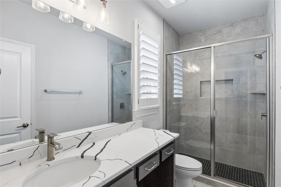 Modern bathroom featuring a single vanity, a sleek glass-enclosed shower, and a pristine toilet.
