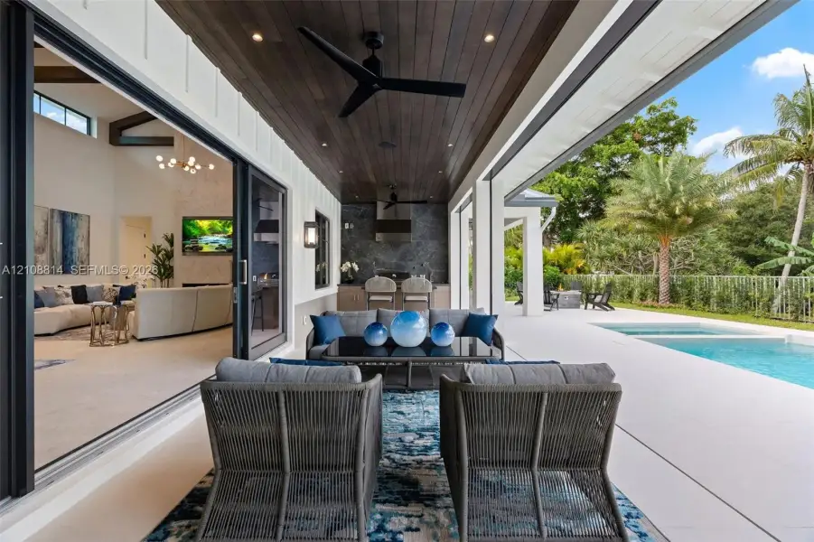 Covered lanai featuring a wood-plank ceiling, recessed lighting, ceiling fans, integrated outdoor kitchen, and multi-panel sliding glass doors opening to a swimming pool and patio area Covered lanai featuring a wood-plank ceiling, recessed lighting, ceiling fans, integrated outdoor kitchen, and multi-panel sliding glass doors opening to a swimming pool and patio area
