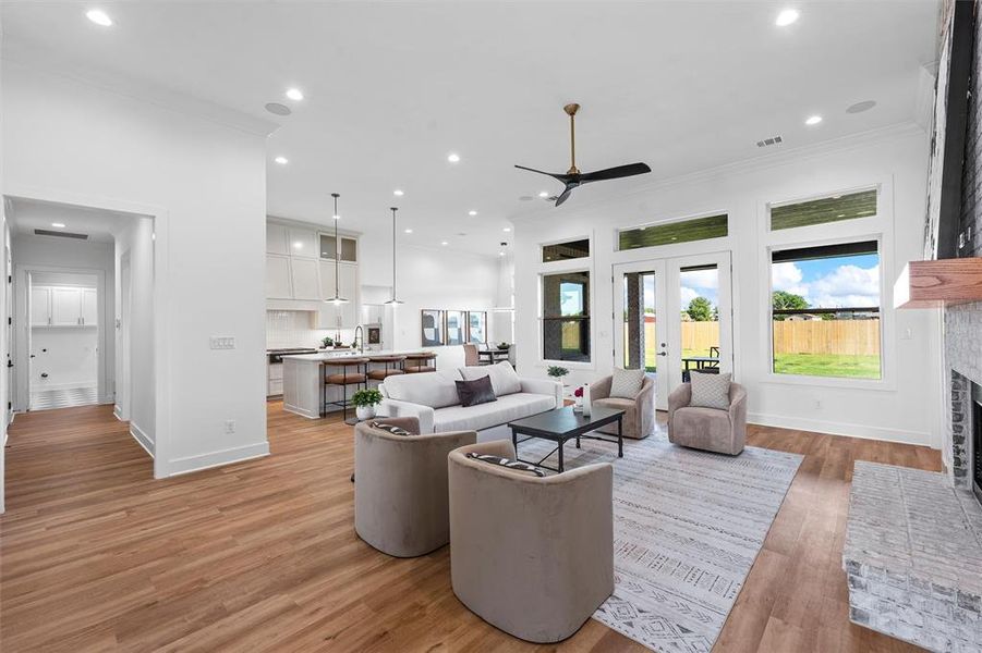 Living room with a ceiling fan, a brick fireplace, french doors, ornamental molding, and light wood-type flooring
