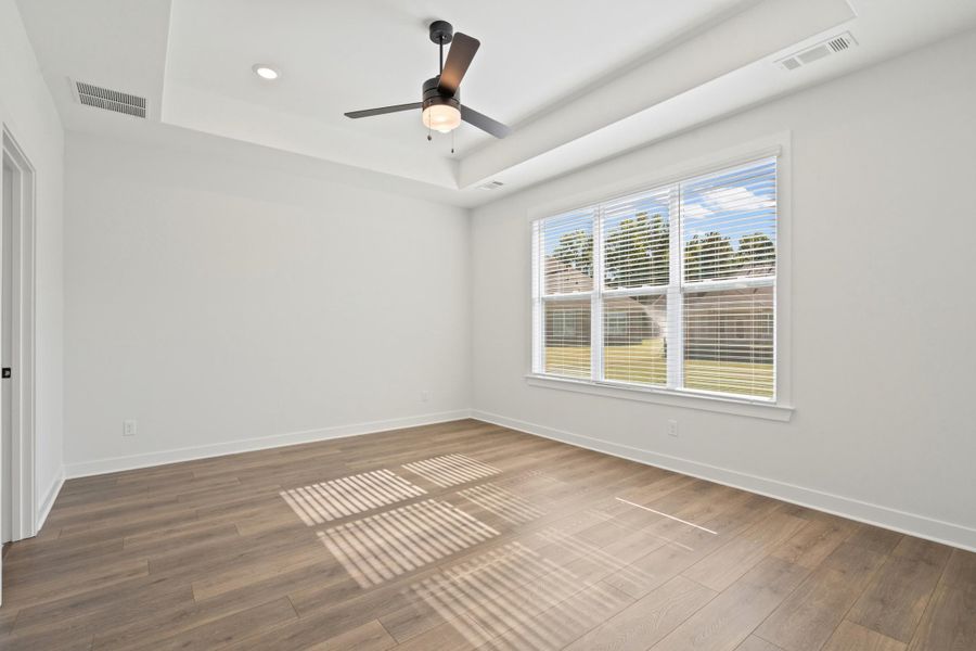 Tray ceiling with recessed lighting, ceiling fan, wood-finish flooring, and a large window with blinds Tray ceiling with recessed lighting, ceiling fan, wood-finish flooring, and a large window with blinds
