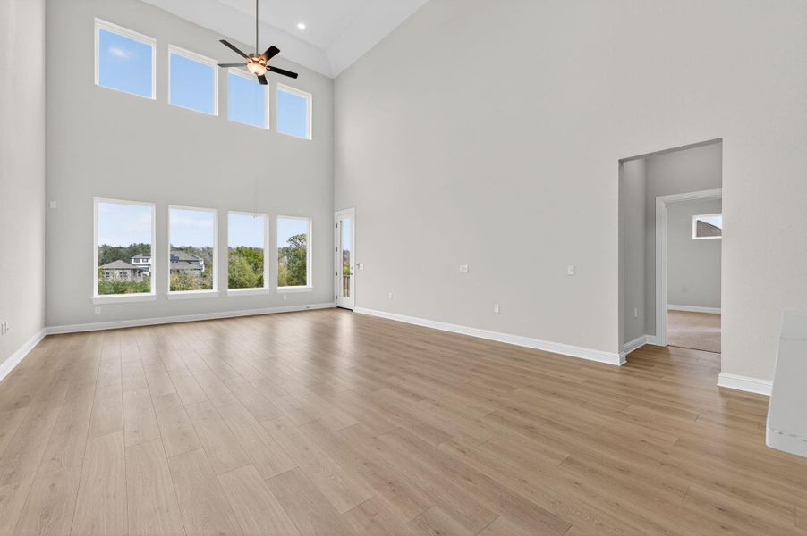 Unfurnished living room featuring plenty of natural light, light wood-type flooring, ceiling fan, and a high ceiling