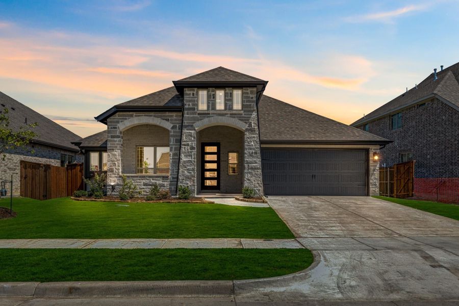 Single-story home with stone exterior, arched entryway, two-car garage, and green front lawn at dusk
