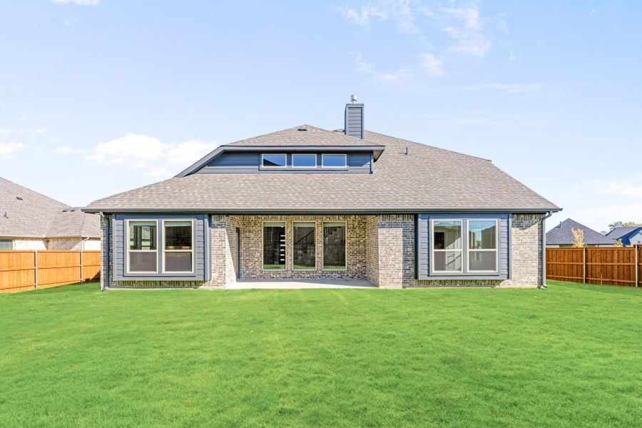Rear exterior of single-story brick home with large windows, hip roof, and fenced green backyard Rear exterior of single-story brick home with large windows, hip roof, and fenced green backyard