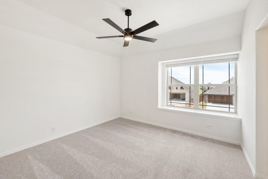 Empty bedroom with gray carpet, black ceiling fan, and large window with neighborhood view