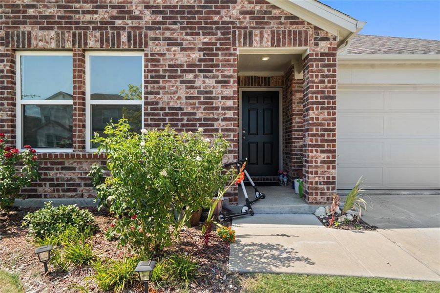 View of exterior entry with brick siding, an attached garage, and a shingled roof