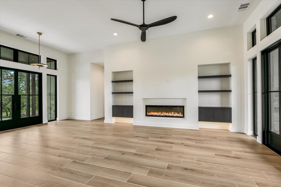 Spacious interior featuring wood-finish flooring, a contemporary linear electric fireplace, and built-in shelving with integrated lighting