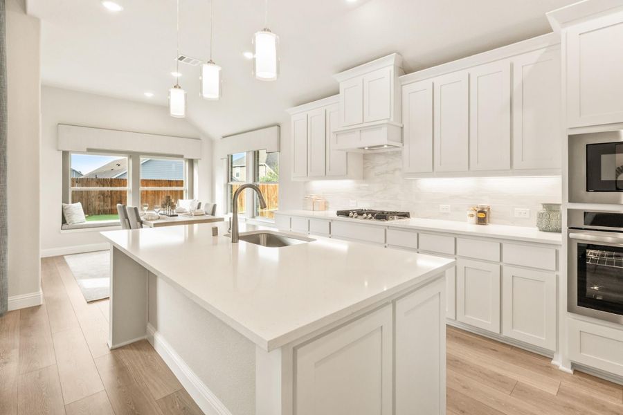 Kitchen with white cabinets, large island with sink, pendant lights, and stainless steel appliances on light hardwood floors Kitchen with white cabinets, large island with sink, pendant lights, and stainless steel appliances on light hardwood floors