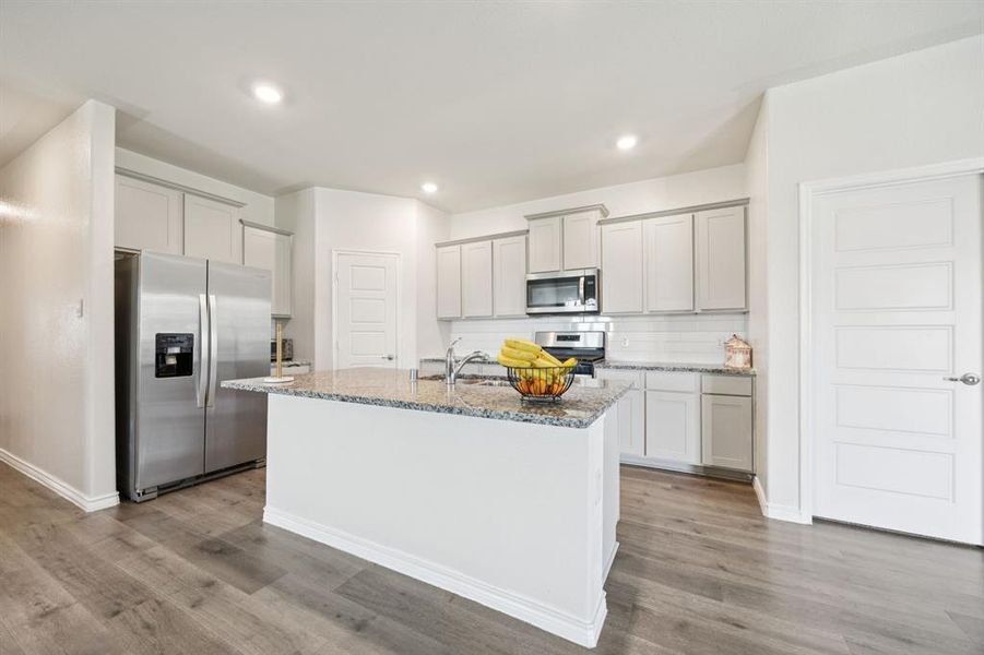 Kitchen featuring light stone countertops, stainless steel appliances, decorative backsplash, an island with sink, and recessed lighting