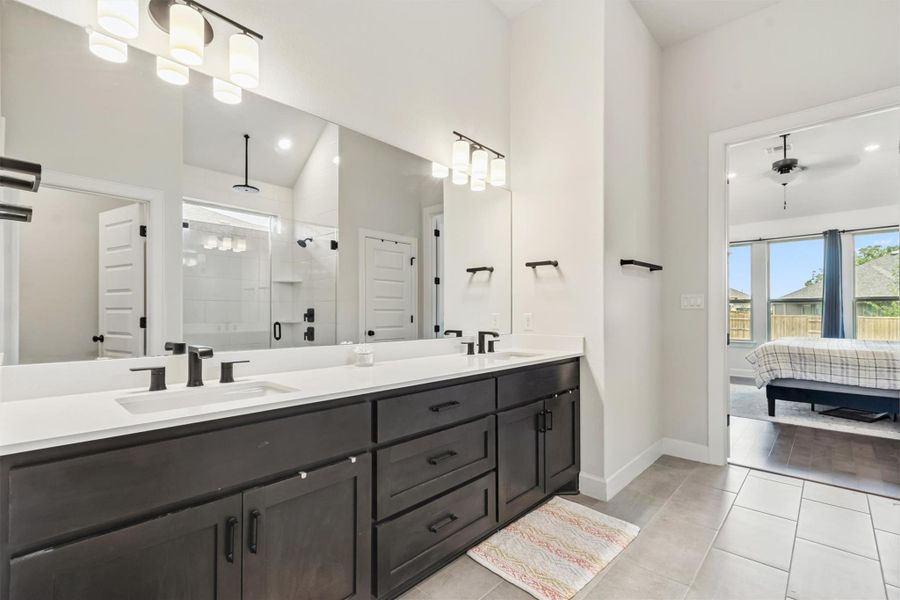 Ensuite bathroom featuring a shower stall, double vanity, light tile patterned floors, and a ceiling fan Ensuite bathroom featuring a shower stall, double vanity, light tile patterned floors, and a ceiling fan