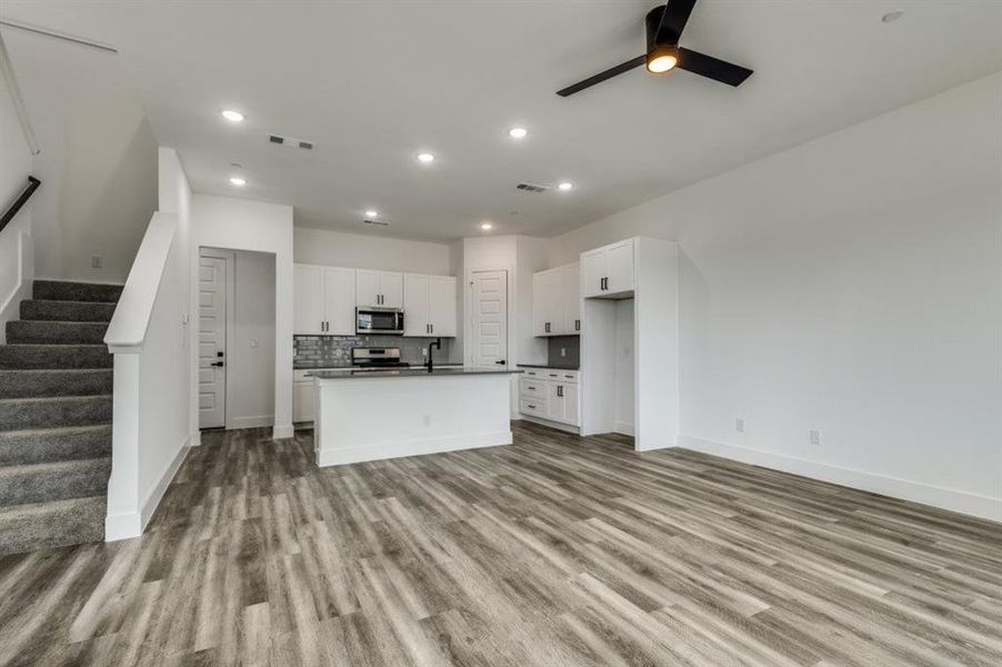 Kitchen featuring appliances with stainless steel finishes, light wood-type flooring, ceiling fan, a center island with sink, and white cabinets