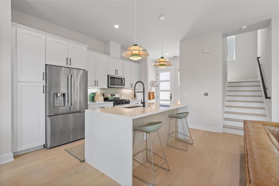 A pristine kitchen features sleek stainless steel appliances, an inviting island with a breakfast bar, and polished hardwood flooring. A pristine kitchen features sleek stainless steel appliances, an inviting island with a breakfast bar, and polished hardwood flooring.
