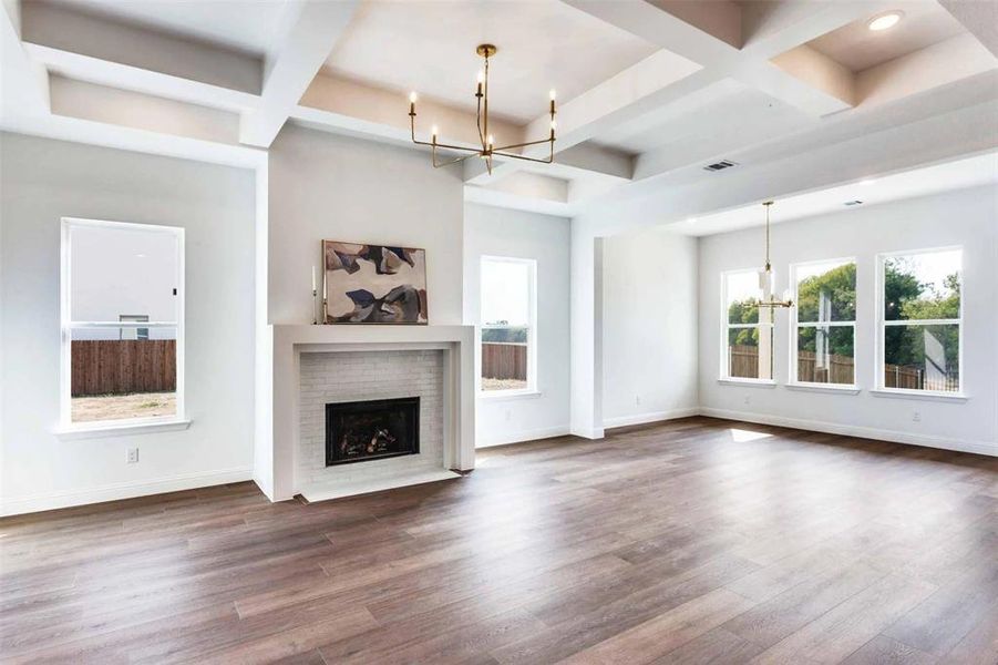 Unfurnished living room with a chandelier, coffered ceiling, beam ceiling, wood finished floors, and a brick fireplace