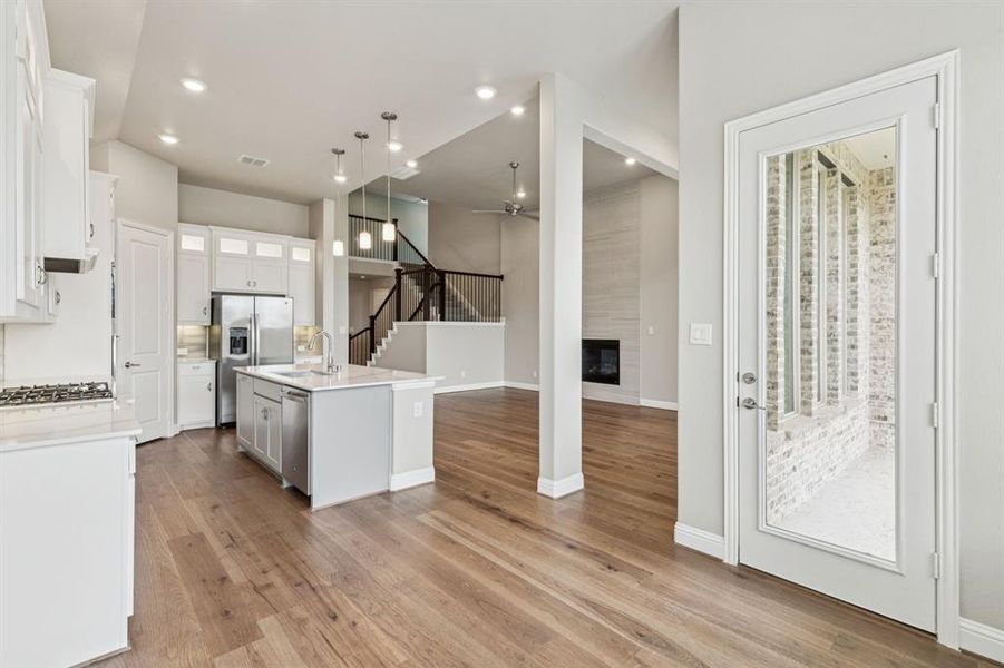 Kitchen featuring stainless steel appliances, a ceiling fan, a tile fireplace, light countertops, and light wood-type flooring