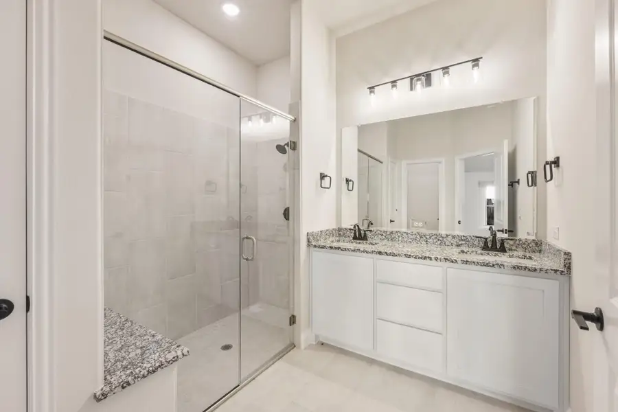 Bathroom with glass walk-in shower, double vanity, granite countertops, and white cabinets