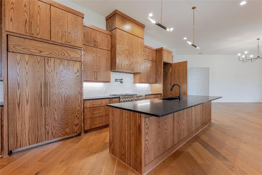 Kitchen featuring a center island with sink, paneled refrigerator, light wood-type flooring, dark stone counters, and decorative backsplash