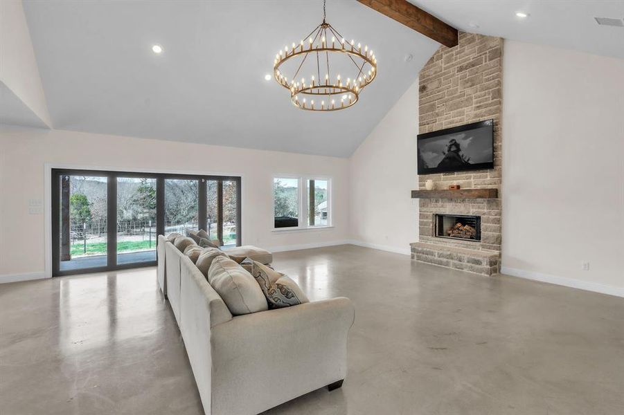 Living room featuring a stone fireplace, concrete floors, and a chandelier Living room featuring a stone fireplace, concrete floors, and a chandelier
