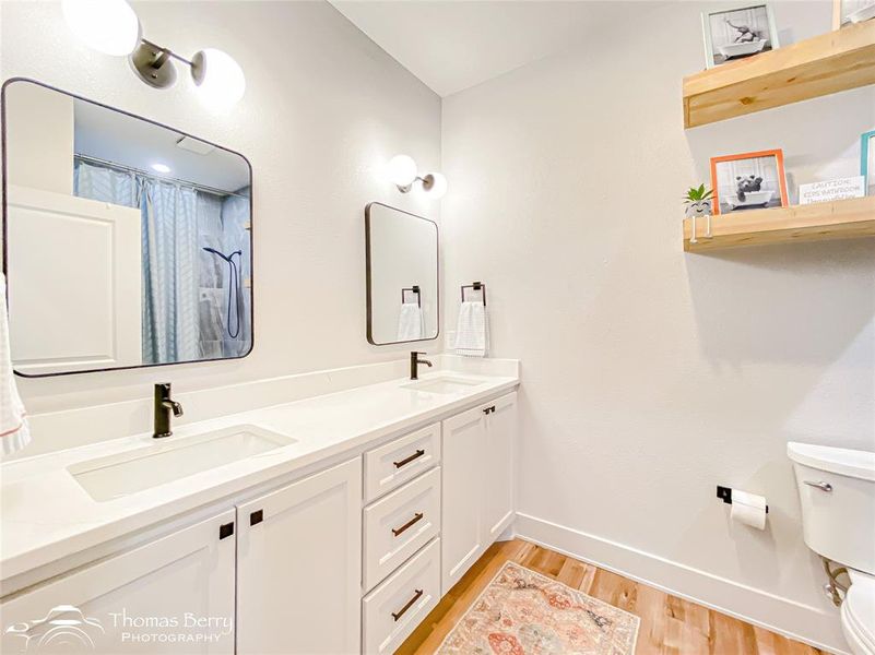 Secondary bathroom with dual sinks, storage, modern shelving.