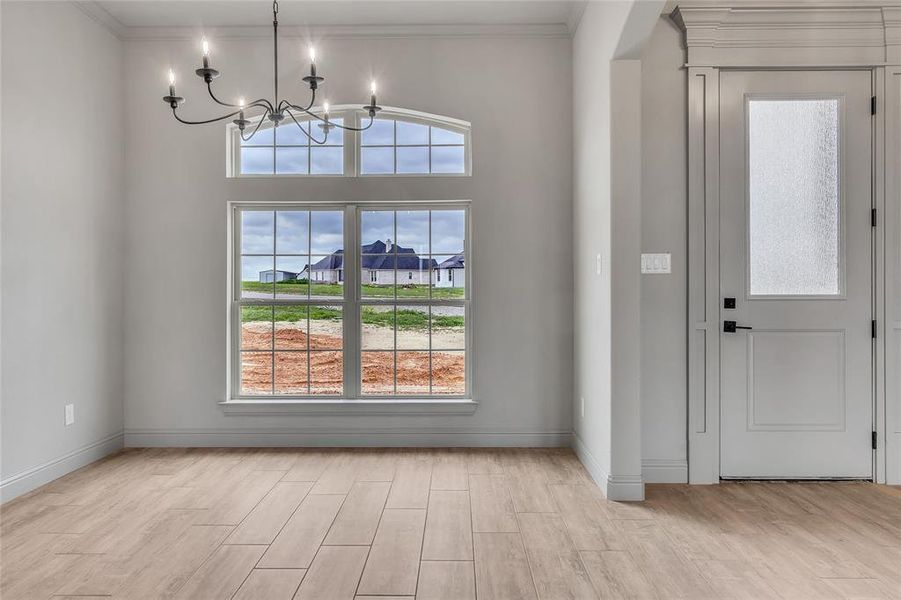 Entryway with ornamental molding, an inviting chandelier, light hardwood / wood-style floors, and a wealth of natural light