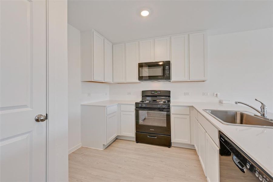 Kitchen featuring sink, light hardwood / wood-style flooring, white cabinets, and black appliances