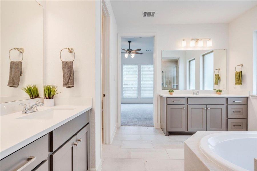 Spacious bathroom featuring dual vanities with gray cabinetry and white countertops, a large mirror, and a built-in bathtub