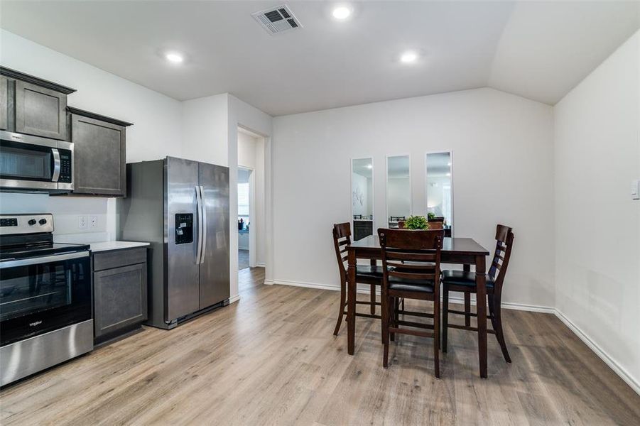 Kitchen with stainless steel appliances, visible vents, vaulted ceiling, and light wood-style flooring