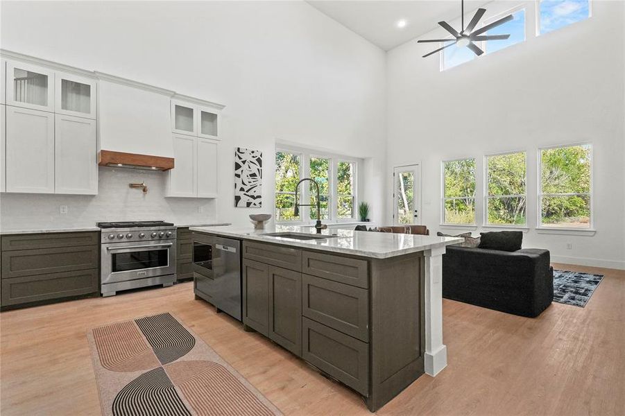 Kitchen with white cabinetry, healthy amount of natural light, stainless steel appliances, light wood-style flooring, and a high ceiling Kitchen with white cabinetry, healthy amount of natural light, stainless steel appliances, light wood-style flooring, and a high ceiling