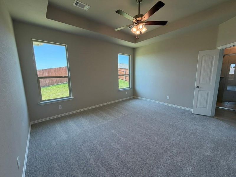 Expansive room featuring a tray ceiling with a ceiling fan light fixture, two large windows, neutral-toned walls, and plush carpet flooring