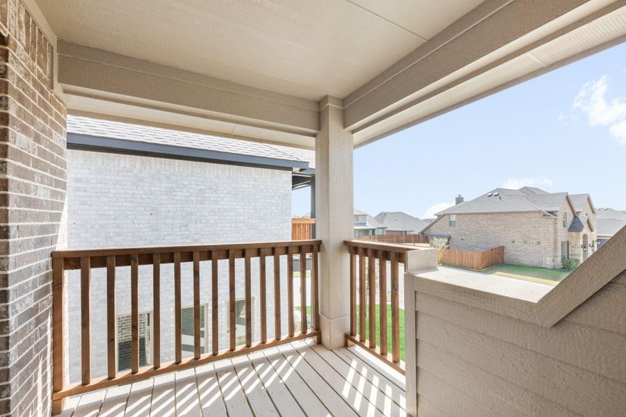 Covered second-floor balcony with wood railing overlooking a residential neighborhood and backyard.