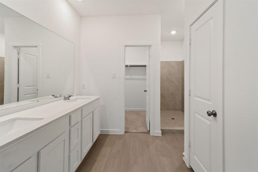 Full bath featuring double vanity, light wood finished floors, walk in shower, recessed lighting, and a walk in closet