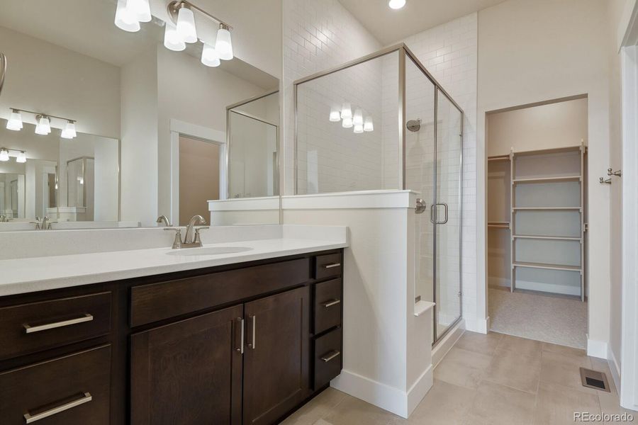 En-suite bath featuring dual vanities, quartz counters, tile flooring, and a shower with bench