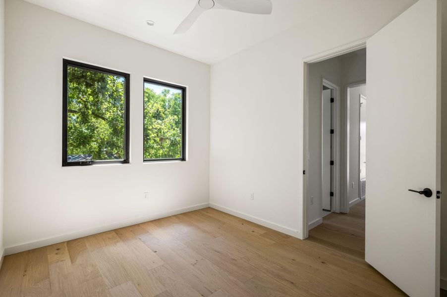 Crisp white walls and warm wood flooring frame leafy outdoor views through dark-trimmed windows.