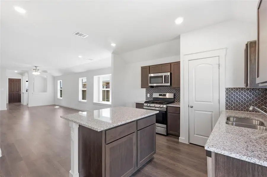 Kitchen with stainless steel appliances, vaulted ceiling, light stone counters, dark wood-type flooring, and a kitchen island