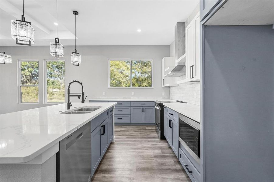 Kitchen with white cabinetry, appliances with stainless steel finishes, decorative light fixtures, sink, and hardwood / wood-style flooring