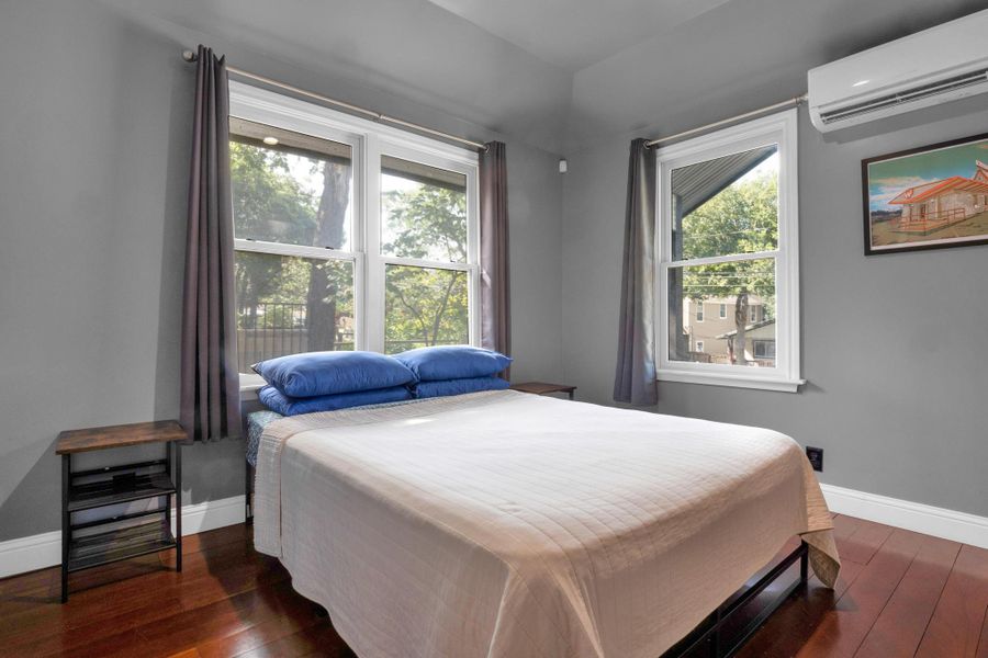 Bedroom featuring a wall unit AC, dark wood-type flooring, and multiple windows