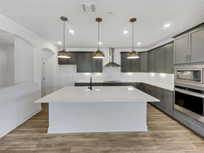 Kitchen with visible vents, a sink, wall chimney range hood, stainless steel appliances, and light countertops