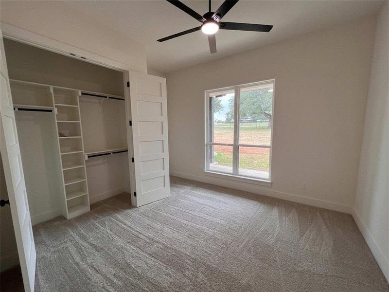 Interior room with light tan patterned carpet flooring, a window with exterior views, and a closet with a built-in shelving system