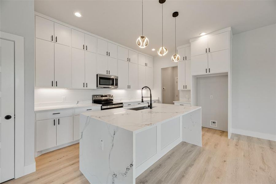 Kitchen with light stone countertops, white cabinetry, pendant lighting, appliances with stainless steel finishes, and an island with sink Kitchen with light stone countertops, white cabinetry, pendant lighting, appliances with stainless steel finishes, and an island with sink