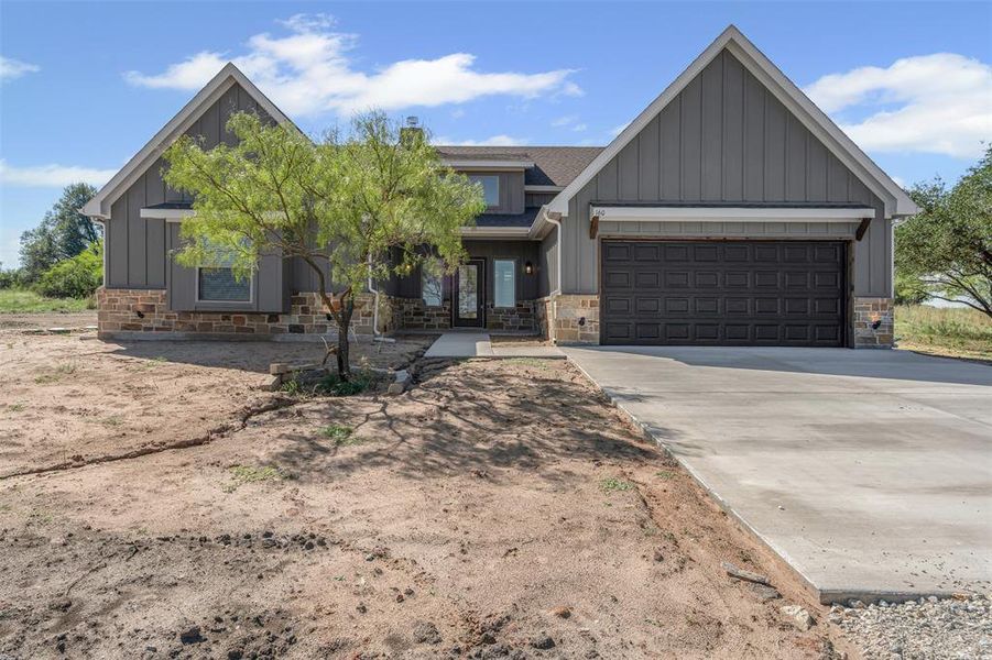 View of front of house featuring board and batten siding, stone siding, driveway, a shingled roof, and a garage