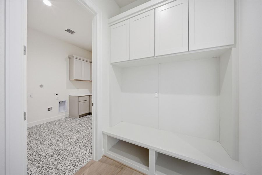 Functional and stylish mudroom with built-in storage conveniently located adjacent to the spacious utility room with designer tile flooring and additional cabinetry.
