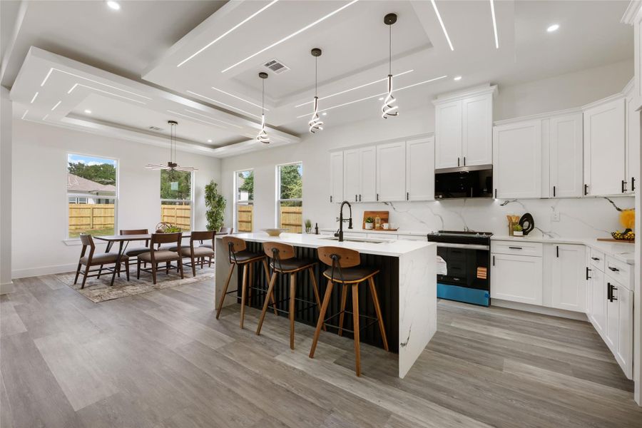 Open-concept kitchen and dining area featuring a waterfall island, white cabinetry, integrated stainless steel appliances, contemporary pendant lighting, and recessed ceiling details